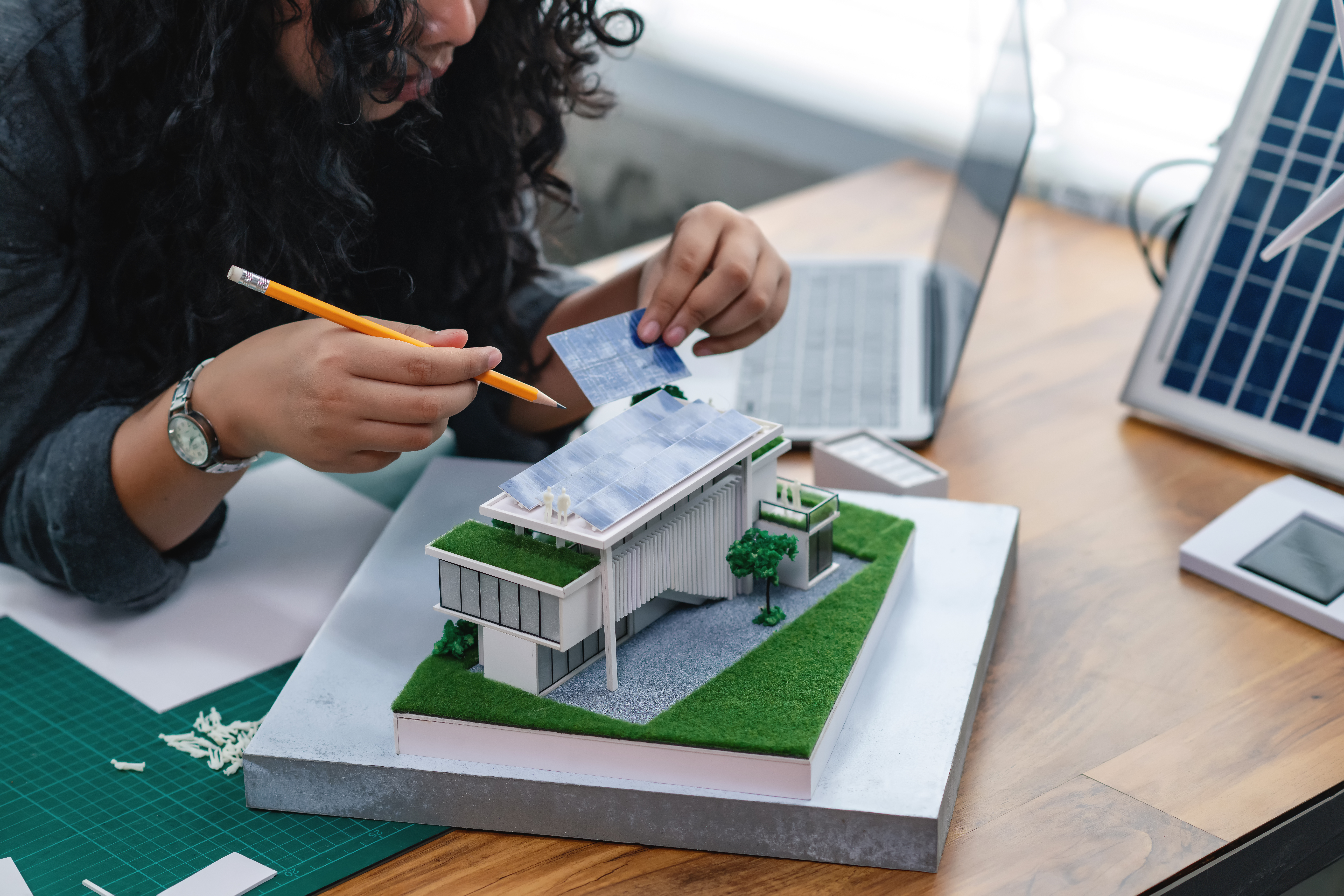 A woman with long brown curly hair holds a pencil and works on a model solar panel