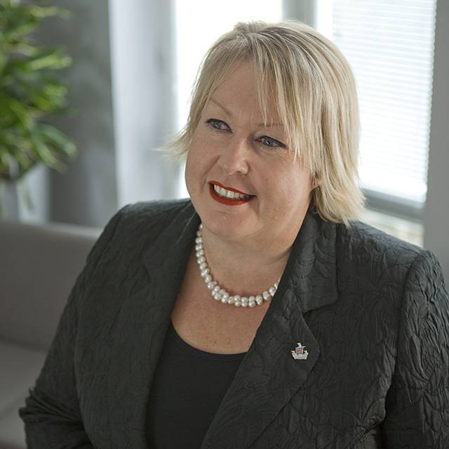 A woman with short blond hair in a grey suit faces the camera