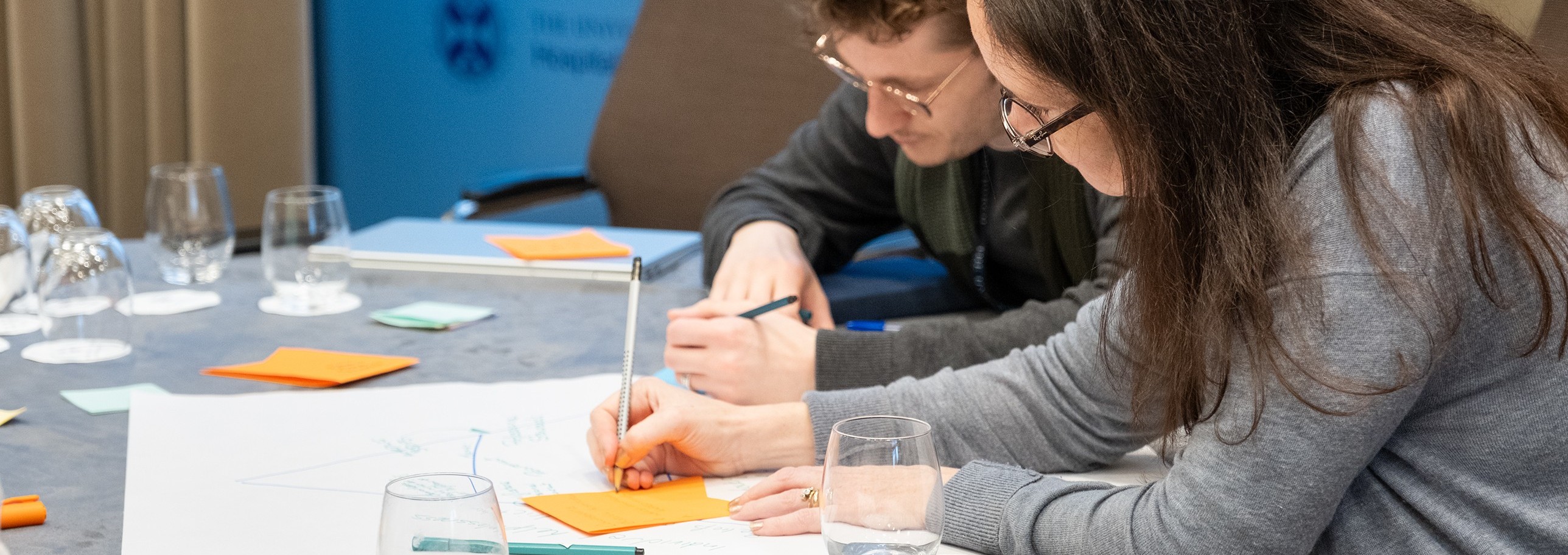 Two people writing on poster paper during a conference session.