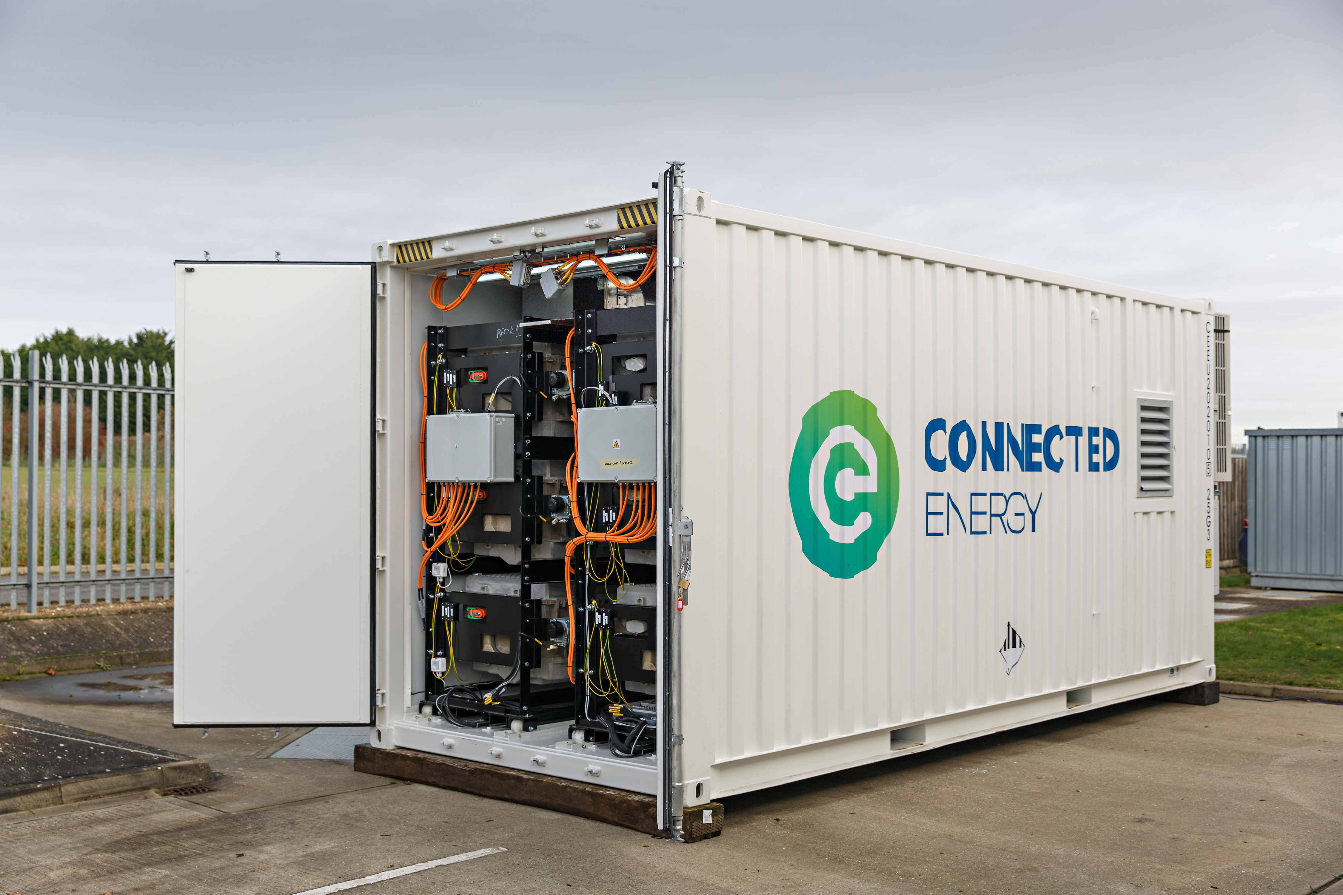 A white shipping container with the words "Connected Energy" displayed on the side. The doors are open to display the battery storage unit within the container."
