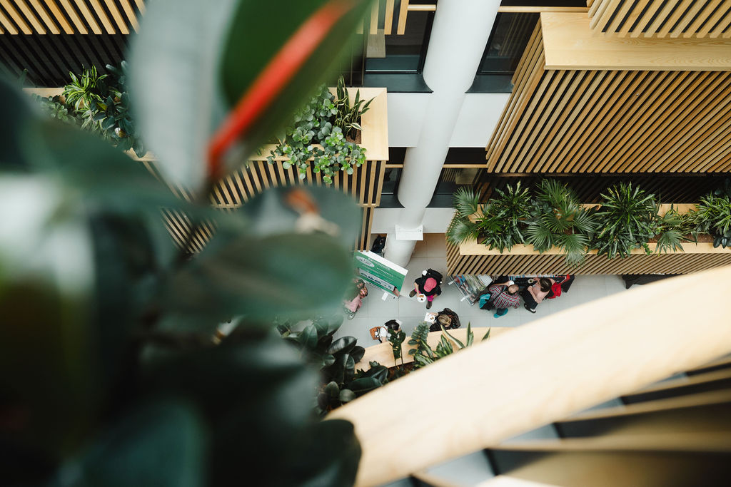 Delegates on a conference floor, viewed through plant foliage. 