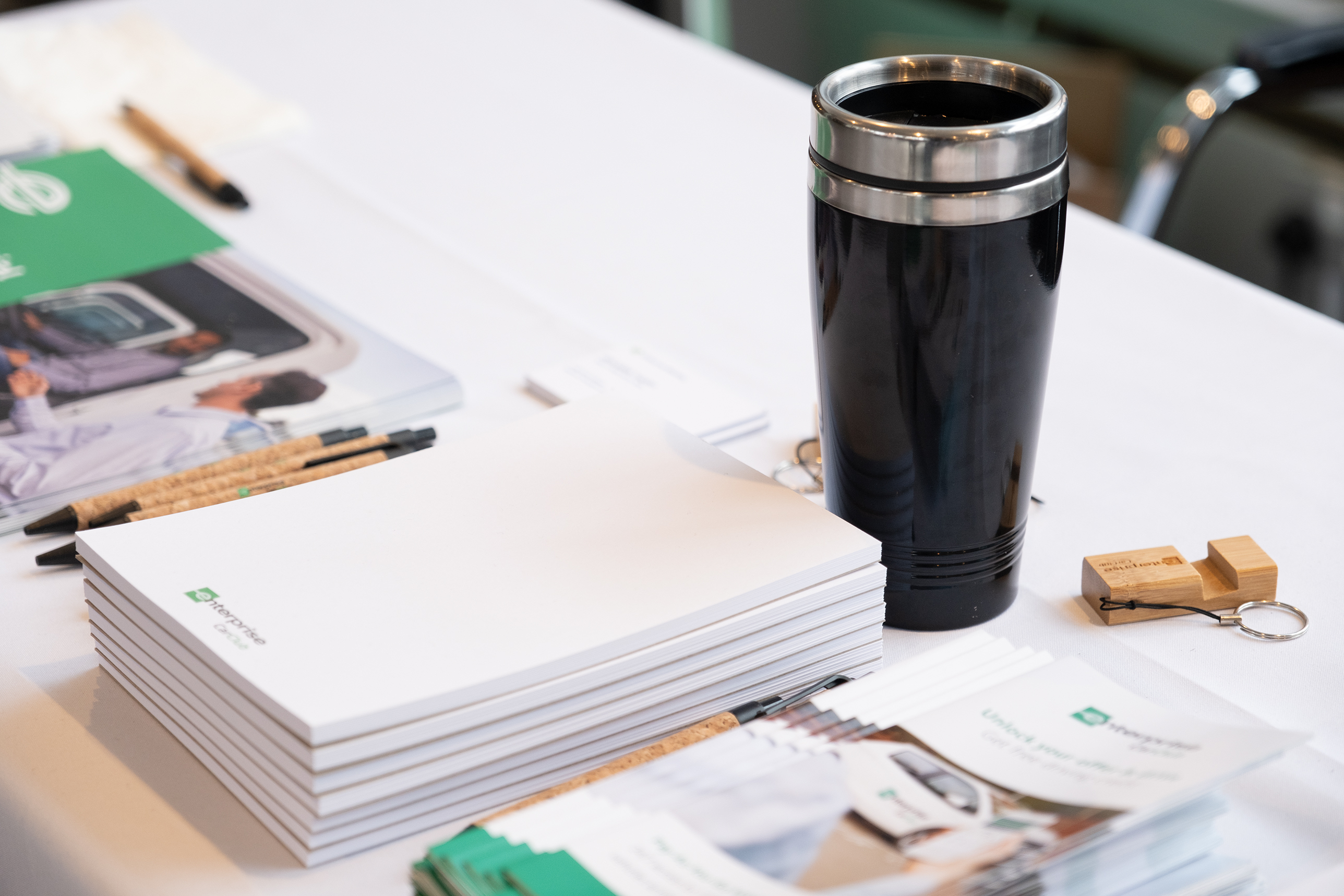 A keep cup alongside various promotional stationery items. 