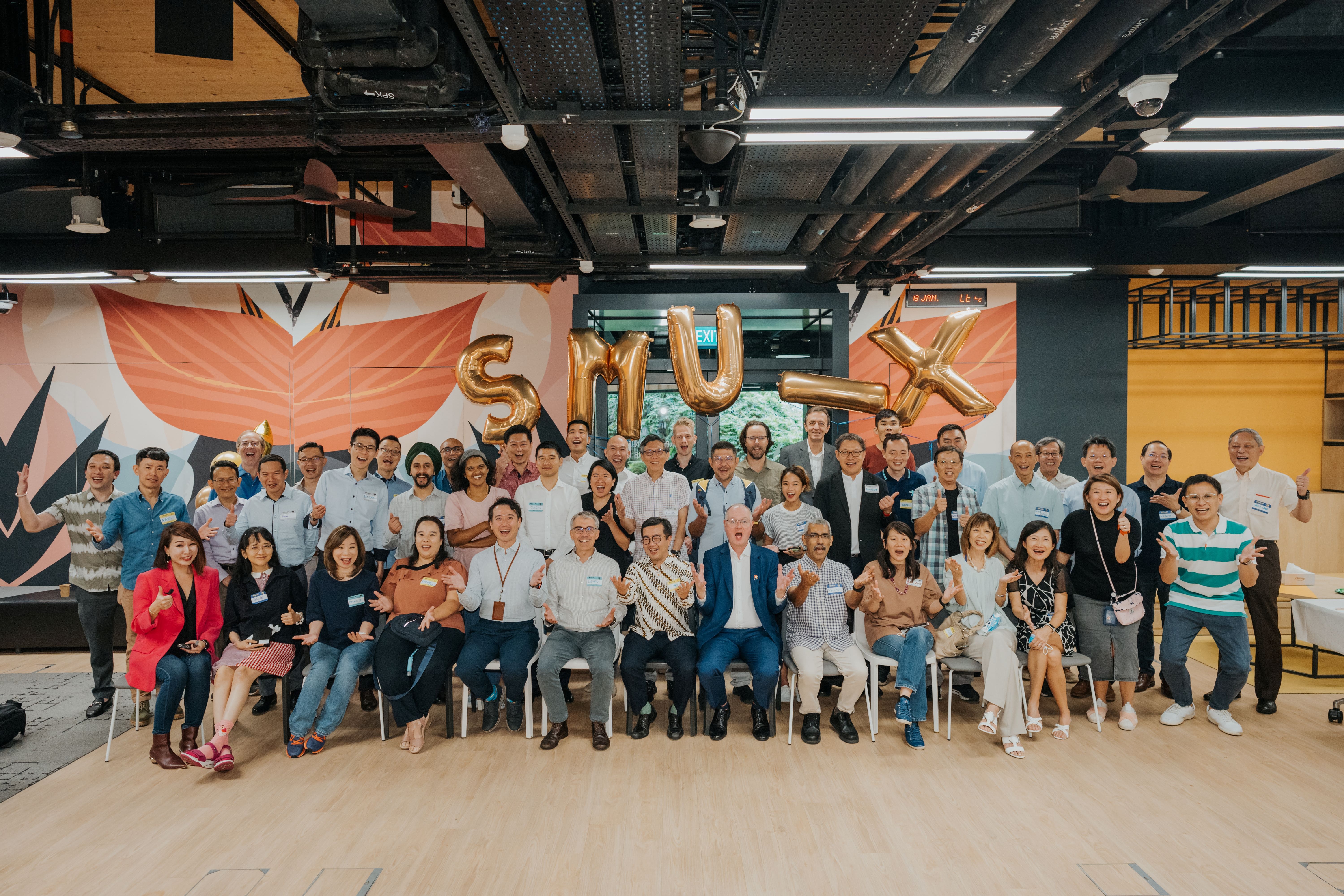A large group of people from Singapore Management University celebrating with SMU balloons in the background