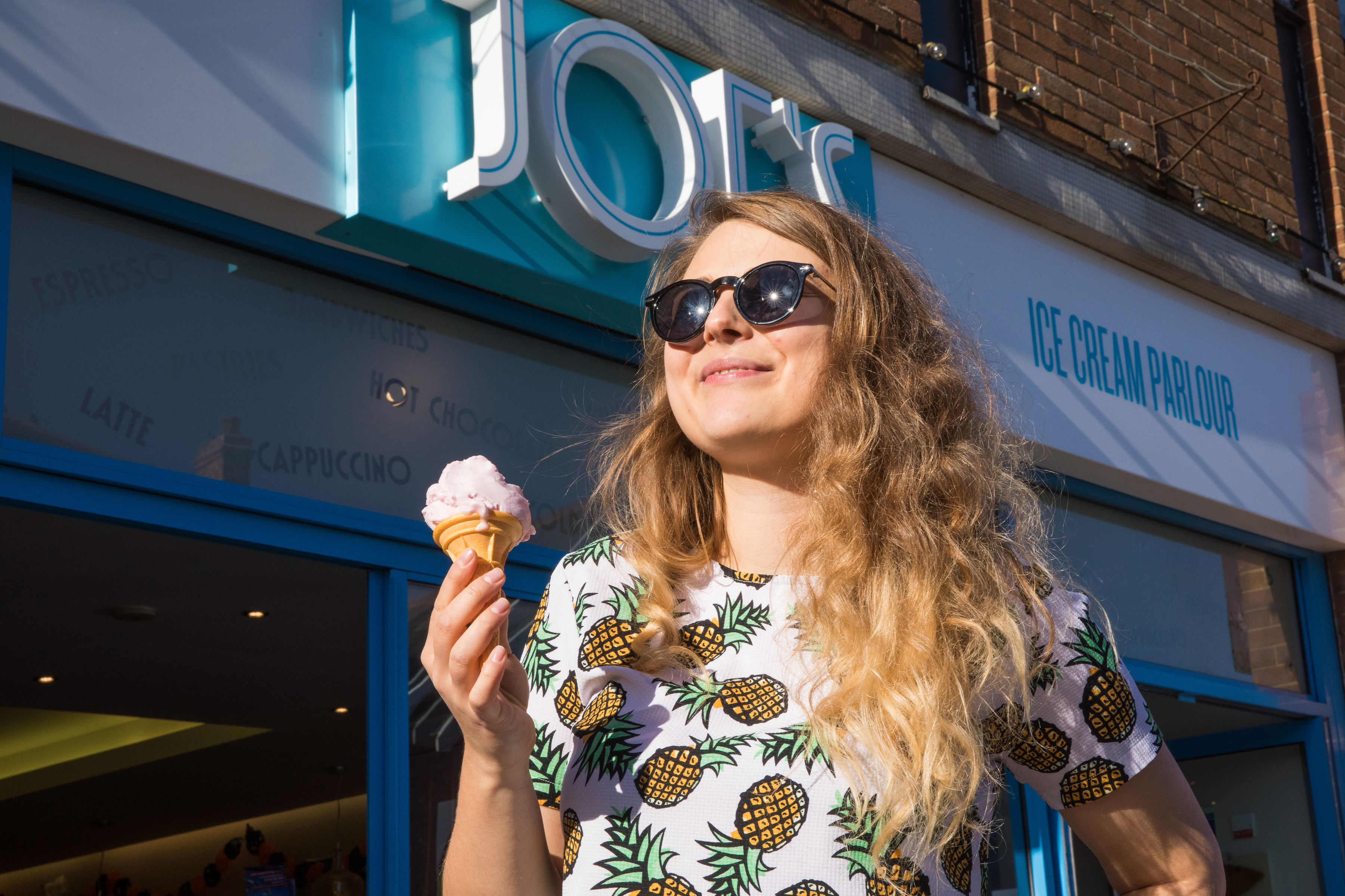 A woman wearing sunglasses and smiling into the sky holds a vanilla ice cream cone